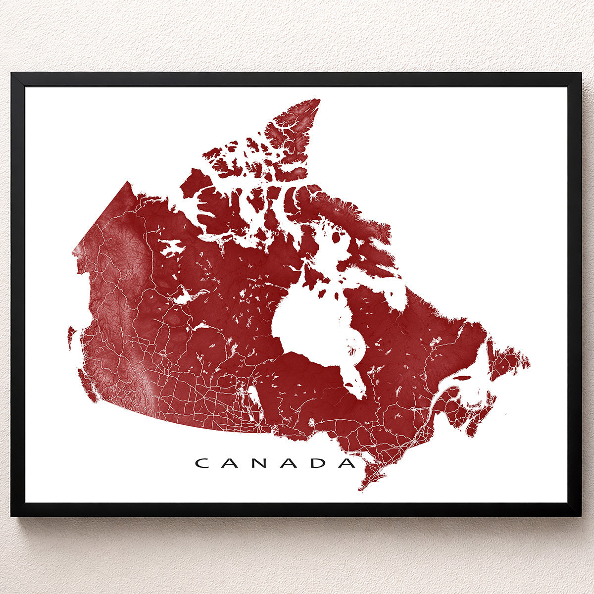 Framed red Canada map print on a wall, showing roads, coastlines, provinces, islands, and detailed map artwork.