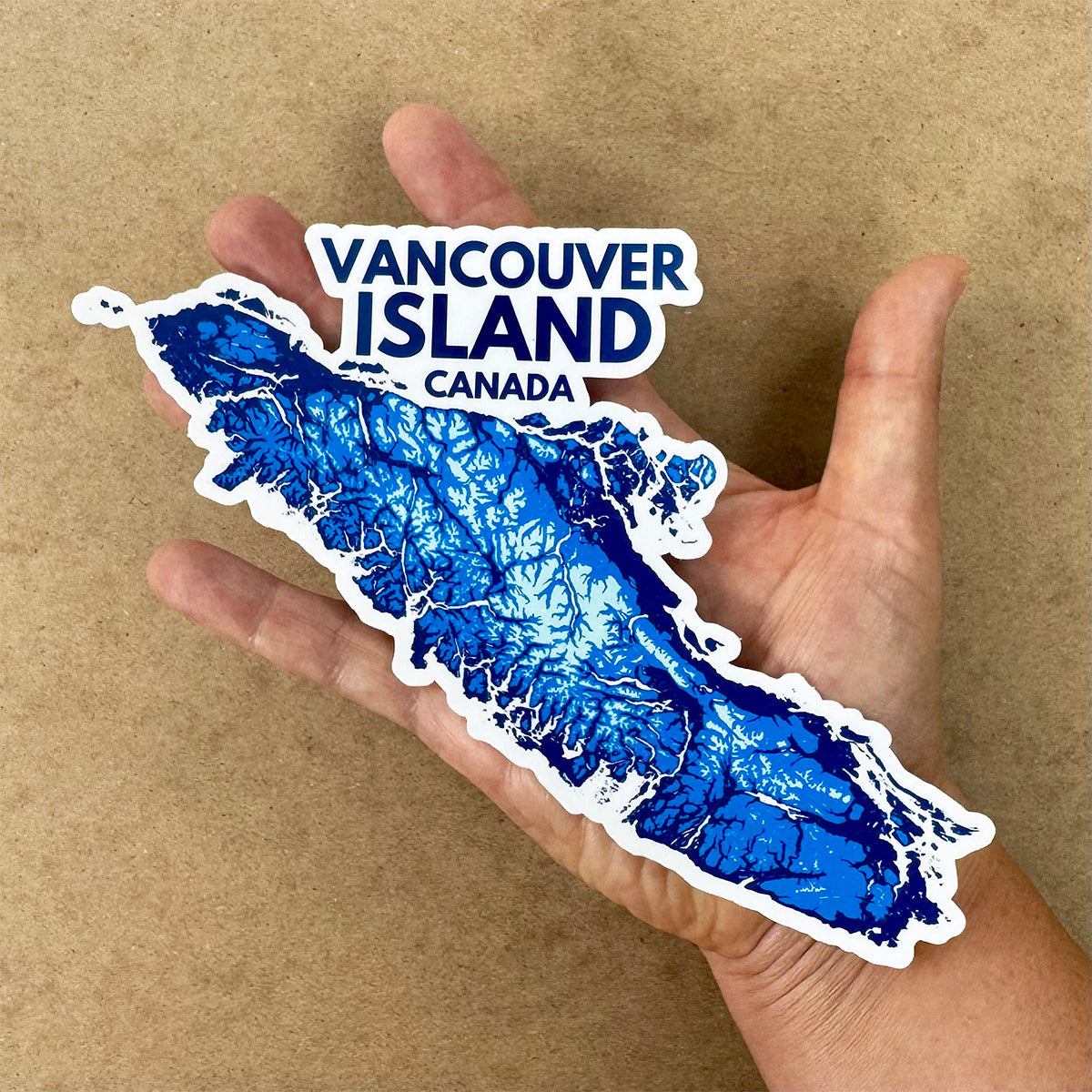 Hand holding a waterproof Vancouver Island map sticker featuring a blue topographic decal design.