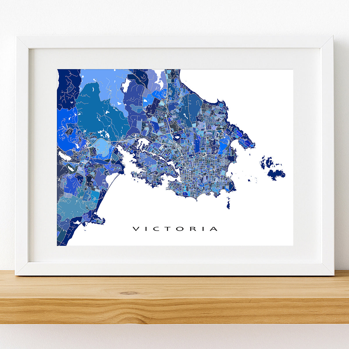 Framed Victoria BC map art print displayed on a shelf, featuring a blue Vancouver Island city map design.