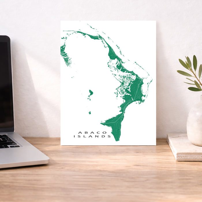 Map of Abaco Islands on a white background, displayed on a wooden desk with a laptop and plant.