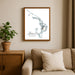 Framed artwork of a map titled 'Abacos' on a wall above a beige sofa with a plant beside it.