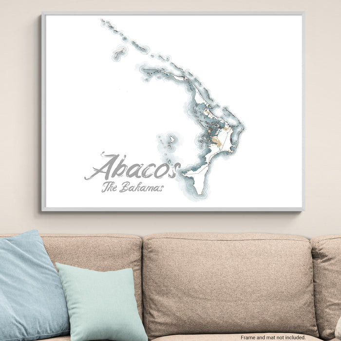 Framed map of Abaco, The Bahamas on a wall above a beige sofa with light blue pillows.