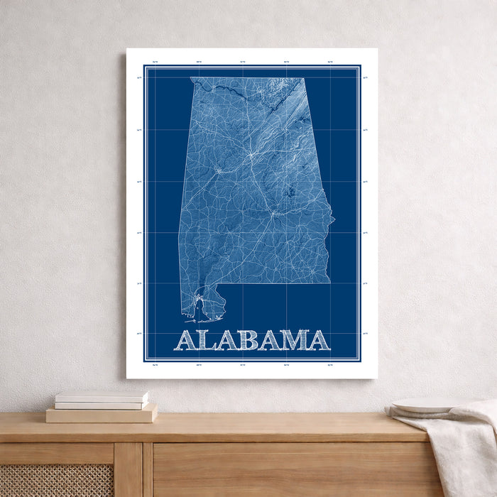 Framed blueprint-style map of Alabama on a wall above a wooden surface.
