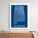 Framed blueprint-style map of Alabama on a wall above a wooden surface.