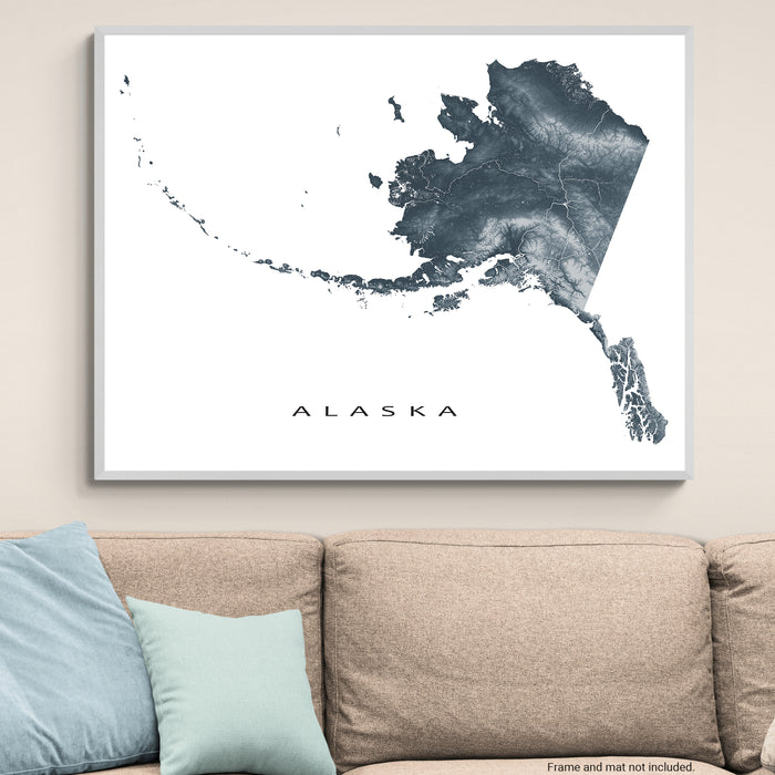 Framed map of Alaska on a wall above a beige sofa with light blue pillows.