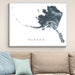 Framed map of Alaska on a wall above a beige sofa with light blue pillows.