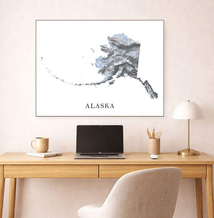 Framed map of Alaska above a desk with a laptop and lamp.