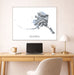 Framed map of Alaska above a desk with a laptop and lamp.