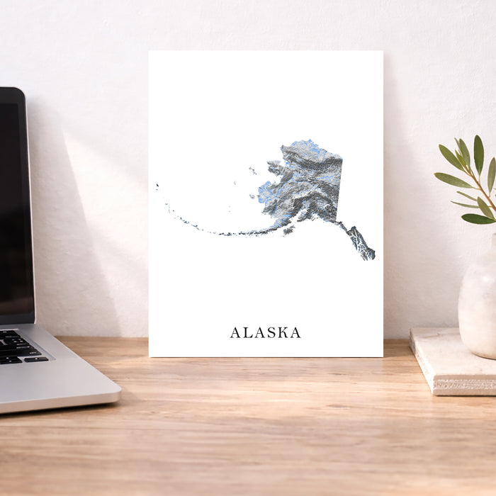 Desk with a laptop, plant, and a poster of Alaska on a white wall.