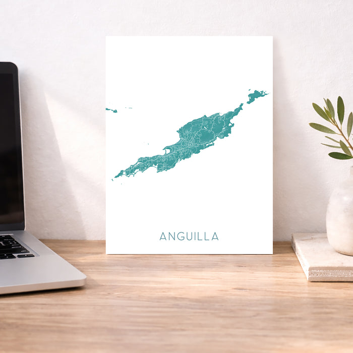 Map of Anguilla on a white background next to a laptop and plant on a wooden desk.