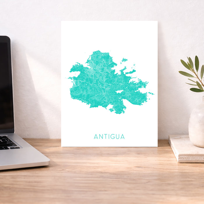 Map of Antigua on a white background displayed on a desk with a laptop and plant.