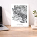 Map of Arizona on a white background displayed on a wooden desk with a laptop and plant.