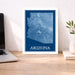 Framed map of Arizona on a desk with a laptop and plant