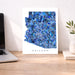 Map of Arizona in blue mosaic design on a white background, placed on a wooden desk with a laptop and plant.