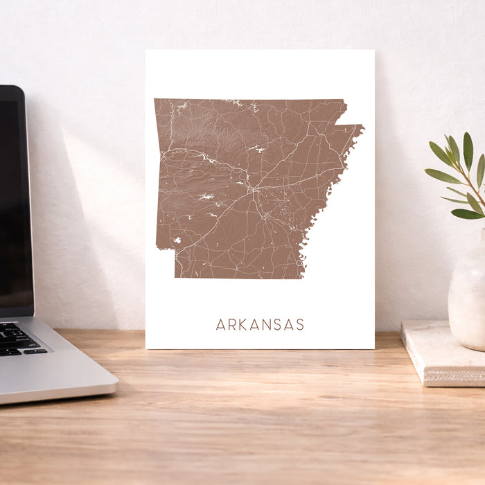Map of Arkansas on a white background next to a laptop on a wooden desk.