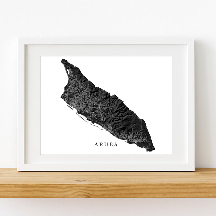 Framed black and white map of Aruba on a wooden shelf.