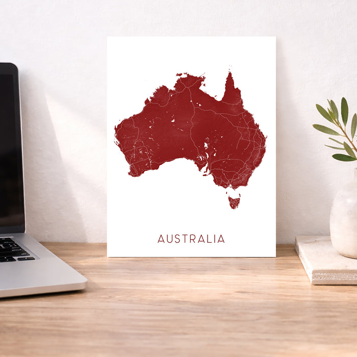 Map of Australia on a white background next to a laptop on a wooden desk.