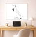 Framed map of The Bahamas above a desk with a laptop and lamp.