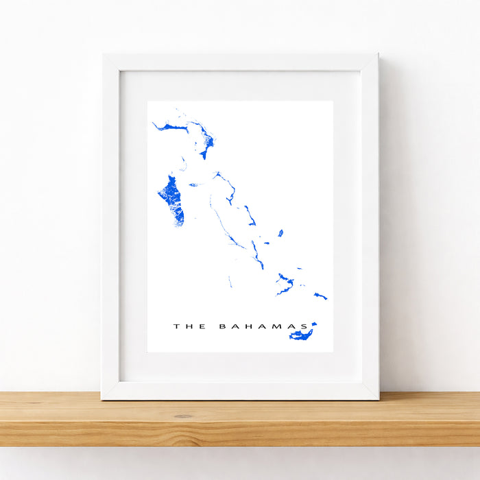 Framed map of The Bahamas on a white wall with a wooden shelf.