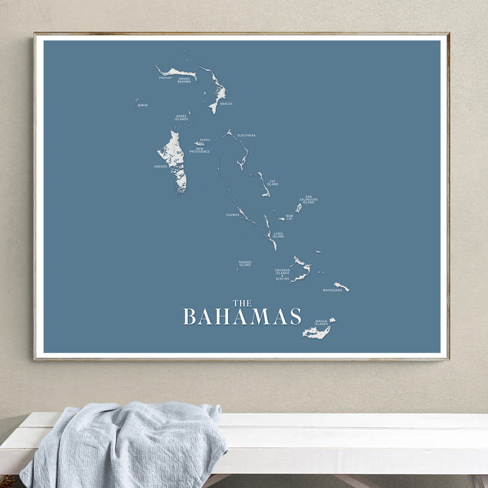 Framed map of The Bahamas on a blue background, hanging on a beige wall above a white surface.