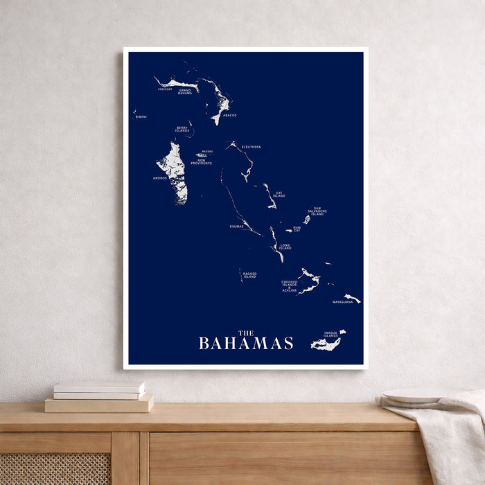 Framed map of The Bahamas on a blue background, displayed on a wooden surface with a neutral wall.