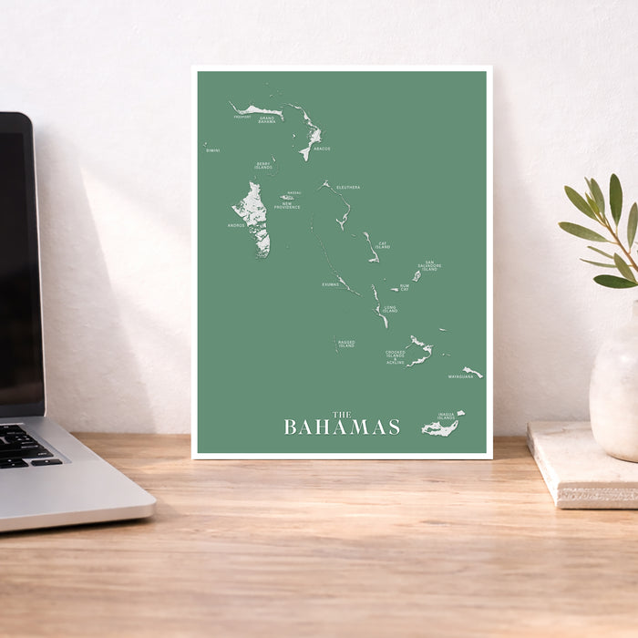 Map of The Bahamas on a green background in a white frame on a desk.