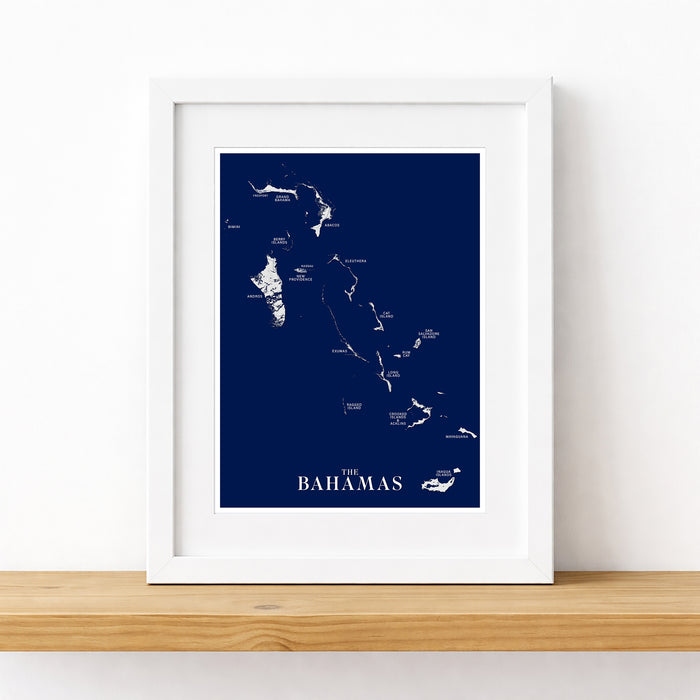 Framed map of The Bahamas on a white wall with a wooden shelf.