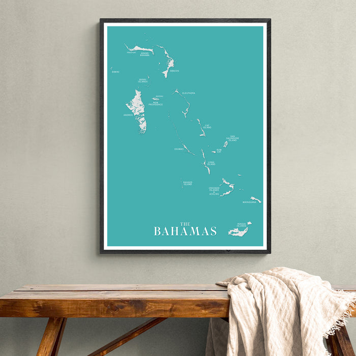 Framed map of The Bahamas on a teal background, displayed on a wall above a wooden bench.