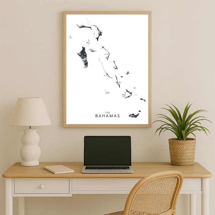 Framed map of The Bahamas above a desk with a laptop, lamp, and plant.