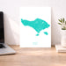 Teal map of Bali on a white poster on a desk with a laptop and plant.