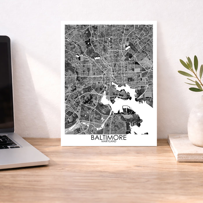 Framed map of Baltimore on a desk with a laptop and plant.