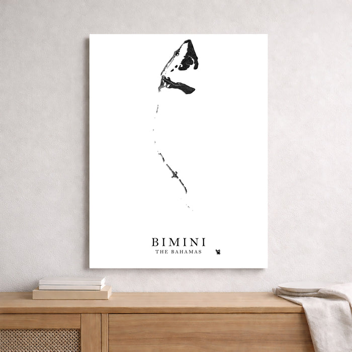 A minimalist black and white shark poster titled 'BIMINI THE BAHAMAS' hanging on a light gray textured wall above a wooden console table with books and a throw blanket.