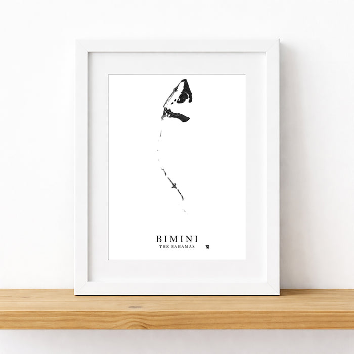 A framed black and white art print featuring a minimalist sketch of a butterfly and the text 'BIMINI THE BARAHAM' at the bottom, displayed on a light wood shelf against a white wall.