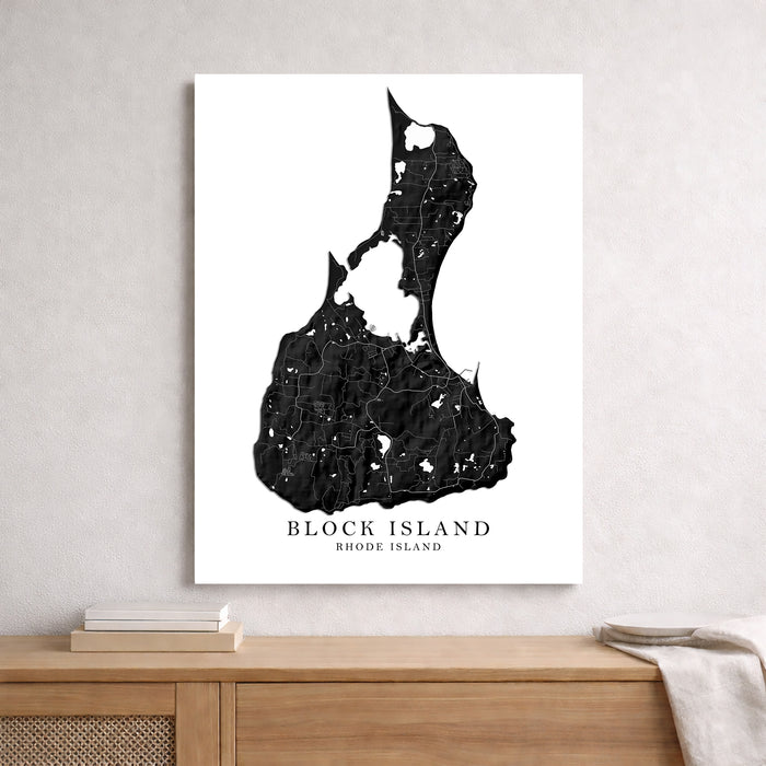 A vertical black-and-white map art print of Block Island, Rhode Island, displayed on a light gray wall above a wooden console table with books and a throw blanket.