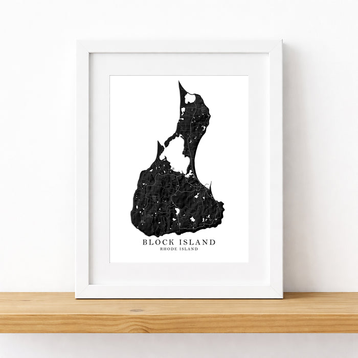 A framed black and white map art print of Block Island, Rhode Island, displayed on a light wood shelf against a white wall.