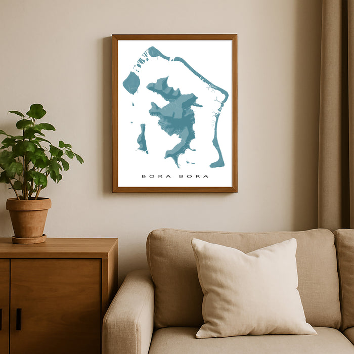 Framed map of Bora Bora on a wall above a beige sofa with a plant beside it.