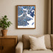 Framed map of Boston on a wall above a beige sofa with a plant beside it.