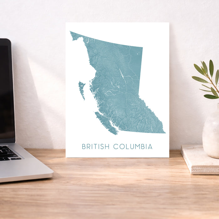 Map of British Columbia on a desk with a laptop and plant