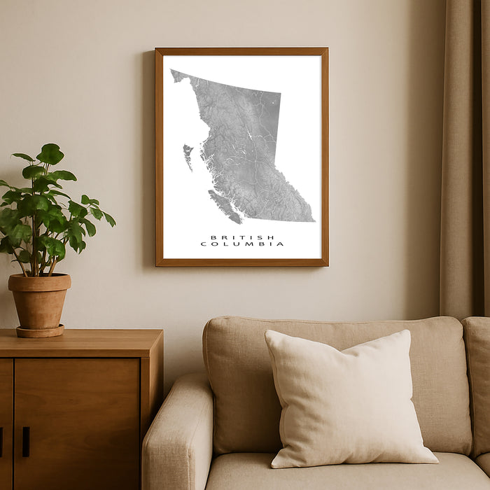 Framed map of British Columbia on a wall above a beige sofa with a plant beside it.
