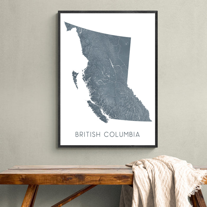 Framed map of British Columbia on a wall above a wooden bench.