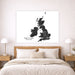 A large square wall art print featuring a black distressed map of the British Isles with the text 'BRITISH ISLES' on a white background, displayed above a neatly made bed in a modern bedroom setting.