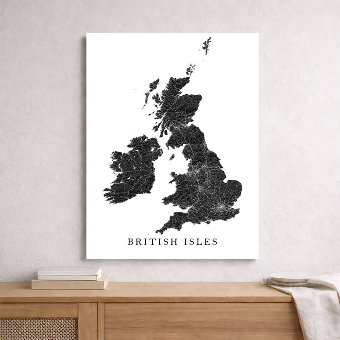 A vertical wall art print showing a black line map of the British Isles on a white background, hanging on a light gray wall above a wooden console table with books and a throw blanket.