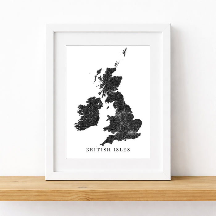 A framed black-and-white map print of the British Isles, leaning against a white wall on a light wood shelf.