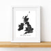 A framed black-and-white map print of the British Isles, leaning against a white wall on a light wood shelf.