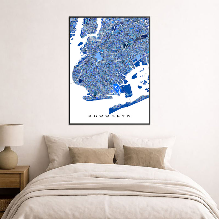 Framed map of Brooklyn on a wall above a bed with beige bedding.