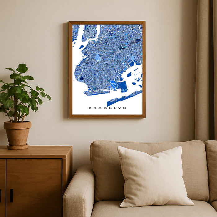 Framed map of Brooklyn on a wall above a beige sofa with a plant beside it.