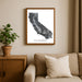 Framed map of California on a wall above a beige sofa with a plant beside it.