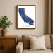Framed map of California on a wall above a beige sofa with a plant beside it.