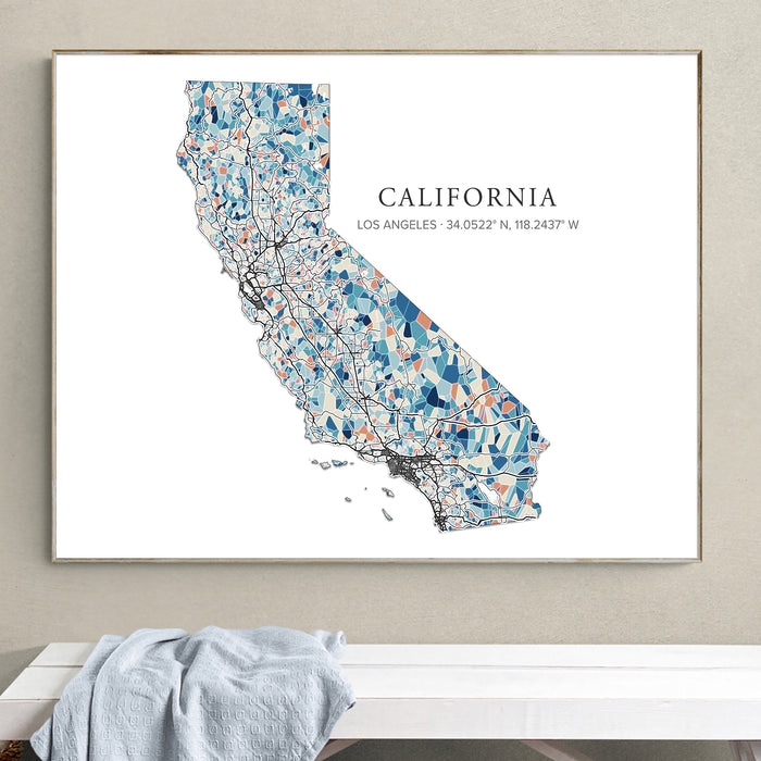 A framed art print of a stylized California map with Los Angeles coordinates, hanging on a beige wall above a white bench with a light blue cloth.