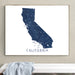 A framed California state map print in dark blue and white, hanging on a beige wall above a white bench with a light blue cloth draped over it.